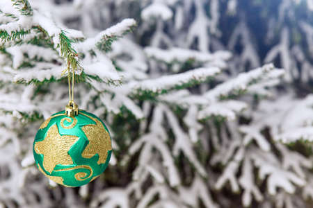Christmas tree toy on the branches of a fir tree covered with snow. Green shiny round toy on the new-year treeの写真素材