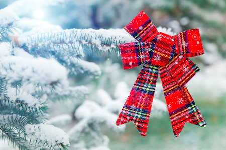 New year decoration red big bow on a snow-covered branch. Christmas tree toy on the branches of a fir tree covered with snow, against the background of a winter forest.