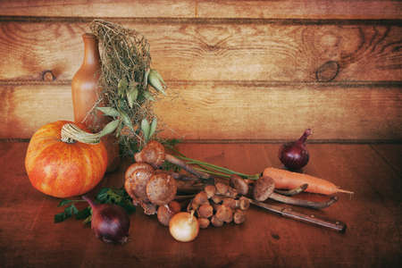 Rural still life of vegetables. On a wooden table is pumpkin mushrooms Armillaria, onions carrots parsley and a knife. Wooden background.の写真素材