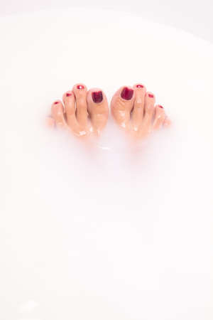 Beautiful legs of a girl with a red manicure in a bath filled with milk. A woman takes a bath. The concept of Spa-relaxing and pedicure salon.の写真素材