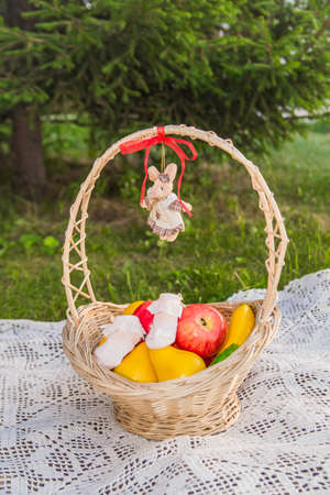 A fruit basket stands in the forest against the background of green Christmas trees. The basket is...