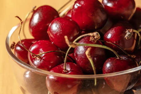 Sweet cherry (black cherry) in a transparent glass cup on a wooden table. Close-up