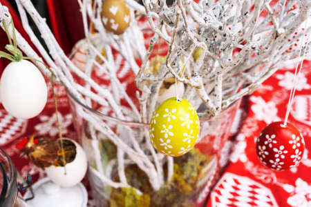 Easter composition with painted eggs hanging on willow branches, on a red table background, outdoor...