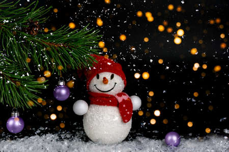 Snowman toy, Christmas balls, background with fir branch, on a black festive background with lights of lanterns and falling snow. Merry Christmas and Happy New Year greeting card with copy space.の写真素材