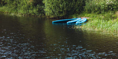 Image of SUP surfboards lying on the river Bank against a background of green trees and bushes. The concept of travel within the country and an active holiday surfingの写真素材