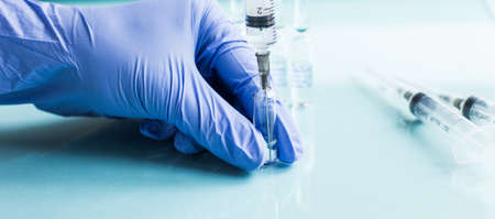 A medical worker in a blue glove fills an injection syringe from an ampoule. The concept of...