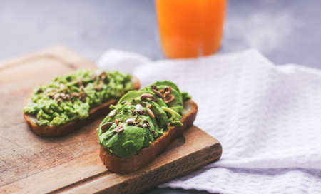 Vegan sandwich with avocado and seeds on a wooden board