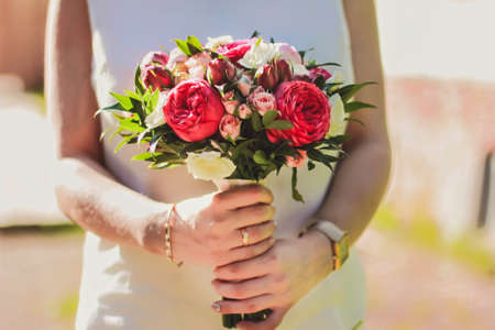 A young girl in white clothes holds a bouquet of white red and pink of roses in her hands