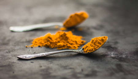 Spices turmeric in a spoon on a dark background, seasonings and healthy food