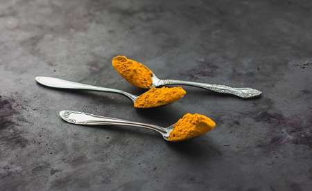 Spices turmeric in a spoon on a dark background, seasonings and healthy foodの写真素材