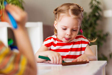 Little girl and boy children at home sit at the table and draw with markers, happy childhood