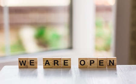 The word "we are open" made of wooden cubes on the background of an open door, End of quarantine a cafe, a local shop, in welcoming guests after the coronavirus outbreak and the shutdown of peopleの写真素材