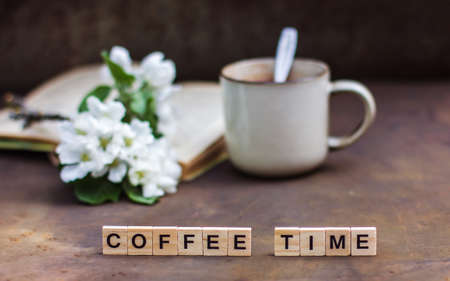 Spring still life on a dark background. The inscription Coffee time A cup of coffee, a book, a...