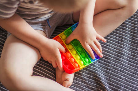 Blonde boy playing with rainbow pop fidget toy. Push bubble fidget sensory toy - washable and reusable stress relief toy. Antistress toy for child with special needs. Mental health conceptの写真素材