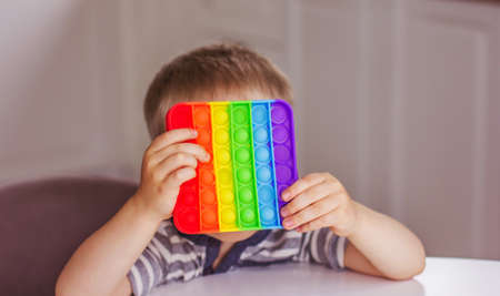 Blonde boy playing with rainbow pop it fidget toy. Push bubble fidget sensory toy - washable and reusable stress relief toy. Antistress toy for child with special needs. Mental health conceptの写真素材