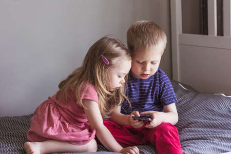 A blond boy and a girl sit on the bed and Using smartphone. Online communication, video...