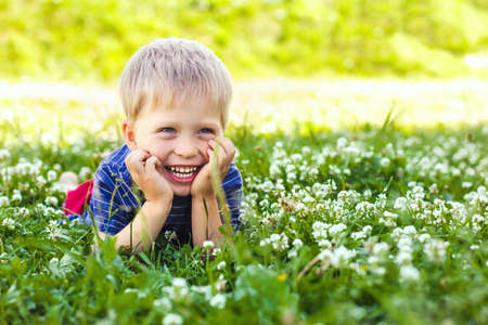 A happy, smiling boy is lying on a green grass lawn. Happy childhood, summer and outdoor recreationの写真素材