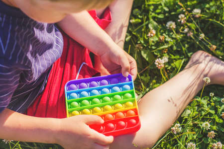 Little boy sitting on a green grass lawn and play silicone toy antistress pop it. Pop it sensory toy. Stress relief. Colorful anti stress silicone sensors toyの写真素材
