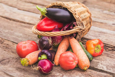 Vegetables in a wicker basket on a wooden background. Fresh crops, farm products, a vegetable garden at home. Copy spaceの写真素材
