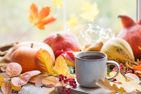 Autumn still life with a beautiful bokeh. Autumn leaves and a cup of hot steaming coffee or tea, orange pumpkins and an autumn harvest. Seasonal, morning coffee, Sunday rest and the concept of still life, mock up layoutの写真素材