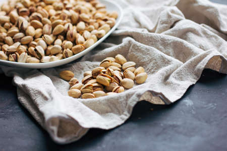 A plate with raw pistachios in a shell on a light tablecloth on a dark gray backgroundの写真素材