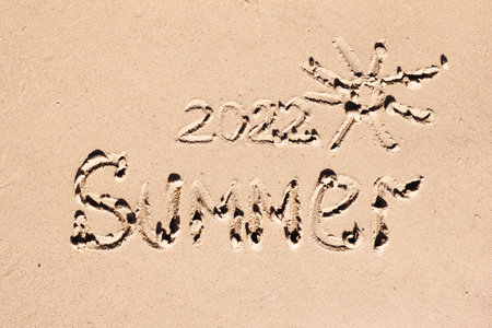 The inscription 2022 and the word summer are drawn on the light sand. New Year symbol, calendar, summer conceptの写真素材