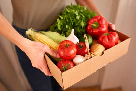 Female hands holding a delivery box filled with fresh organic vegetables and fruitsの写真素材