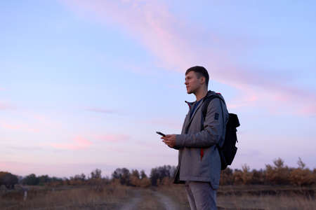 Young man with smartphone walking outdoors in autumn time