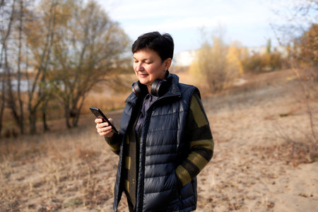 Happy mature woman walking outdoors and using smartphone