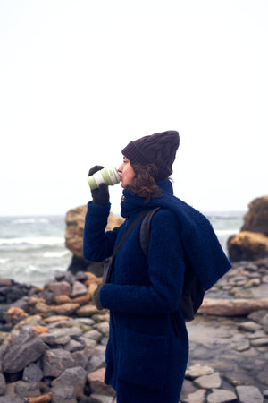 Beautiful caucasian woman walking by the sea and holding reusable eco-friendly cup of coffeeの写真素材