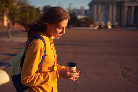 Beautiful caucasian young woman drinking coffee outdoors in yellow sweaterの写真素材