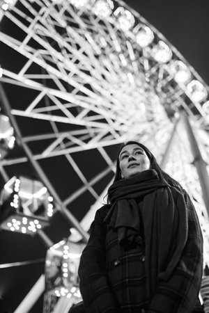 Young beautiful caucasian brunette woman posing by ferris wheel at night. Black and white photos