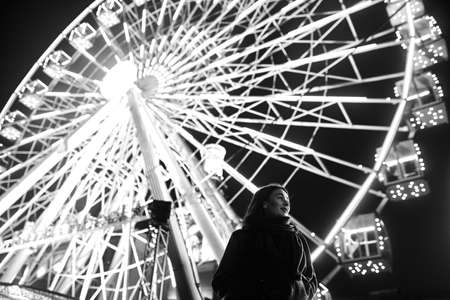 Young beautiful caucasian brunette woman posing by ferris wheel at night.の写真素材