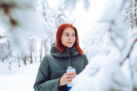 Cheerful girl with red hair in warm clothes playing with snow outdoors near the beautiful forest