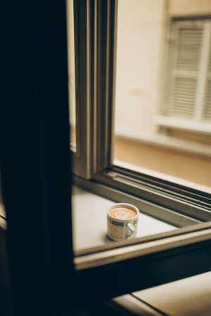 Coffee cup near the window with shutters in Turin, Italy. Enjoy the moment, relax lifestyle. Cozy sunny day. weekend vibesの写真素材
