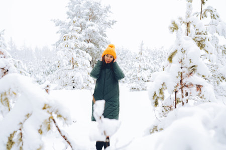 Cheerful girl in warm clothes playing with snow outdoors near the beautiful forest