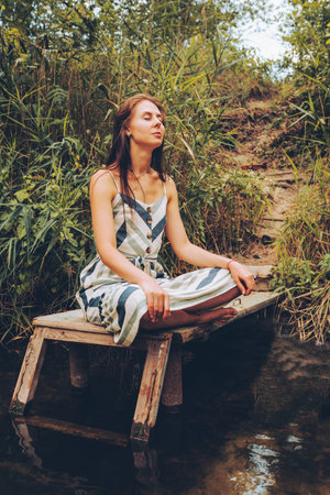 Woman practicing yoga on pier by river.の写真素材