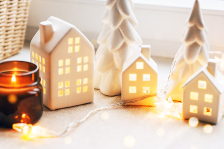 Enjoy a warm holiday ambiance with ceramic house decorations, a candle, and a festive setting.の写真素材