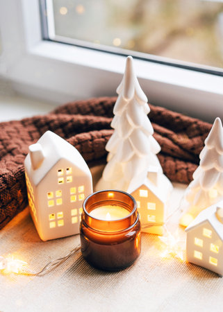 Enjoy a warm holiday ambiance with ceramic house decorations, a candle, and a festive setting.の写真素材