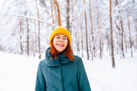 A cheerful woman in a yellow hat and gloves enjoying a snowy day outdoors surrounded by trees.の写真素材