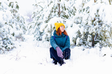 A cheerful woman in a yellow hat and gloves enjoying a snowy day outdoors surrounded by trees.の写真素材
