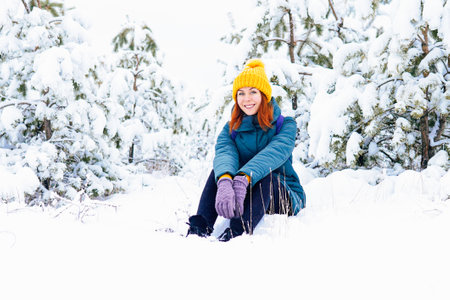 A cheerful woman in a yellow hat and gloves enjoying a snowy day outdoors surrounded by trees.の写真素材