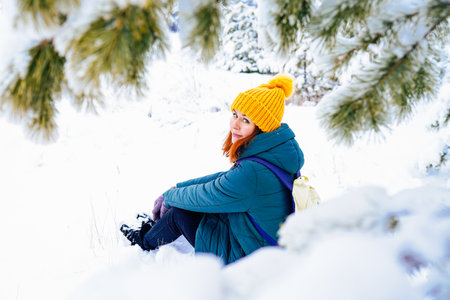 A cheerful woman in a yellow hat and gloves enjoying a snowy day outdoors surrounded by trees.の写真素材