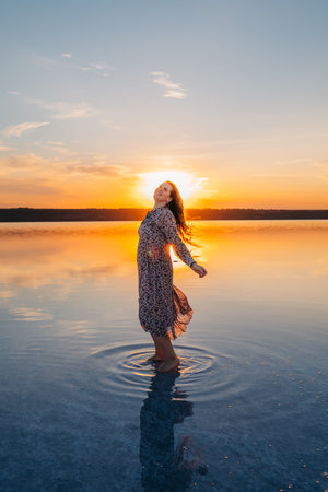 Joyful Woman with Flowing Hair Enjoying a Golden Sunset by the Waterの写真素材