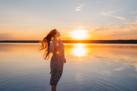 Joyful Woman with Flowing Hair Enjoying a Golden Sunset by the Waterの写真素材