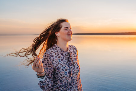 Joyful Woman with Flowing Hair Enjoying a Golden Sunset by the Waterの写真素材