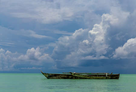One old homemade wooden boat in  the ocean against the horizon at good weather.の写真素材