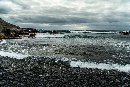 view from a stormy deserted shore to a raging ocean during a storm with a clear horizon line and a gray sky covered with thunderstorm continuous cloudsの写真素材