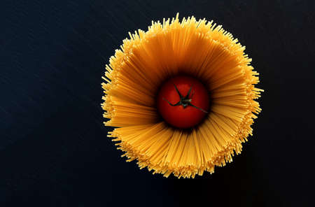 one ripe red tomato in the middle of a bouquet of raw spaghetti top view on a black background in the studioの写真素材