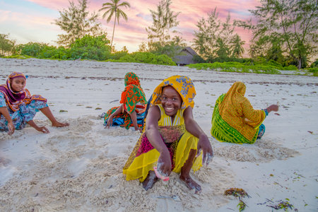 Stone Town, Zanzibar, Tanzania. 27 March 2018. cheerful african girls collect shells on the sandy beach They Playing Outdoors Laughing and Smiling Together (Happiness Symbol)のeditorial素材
